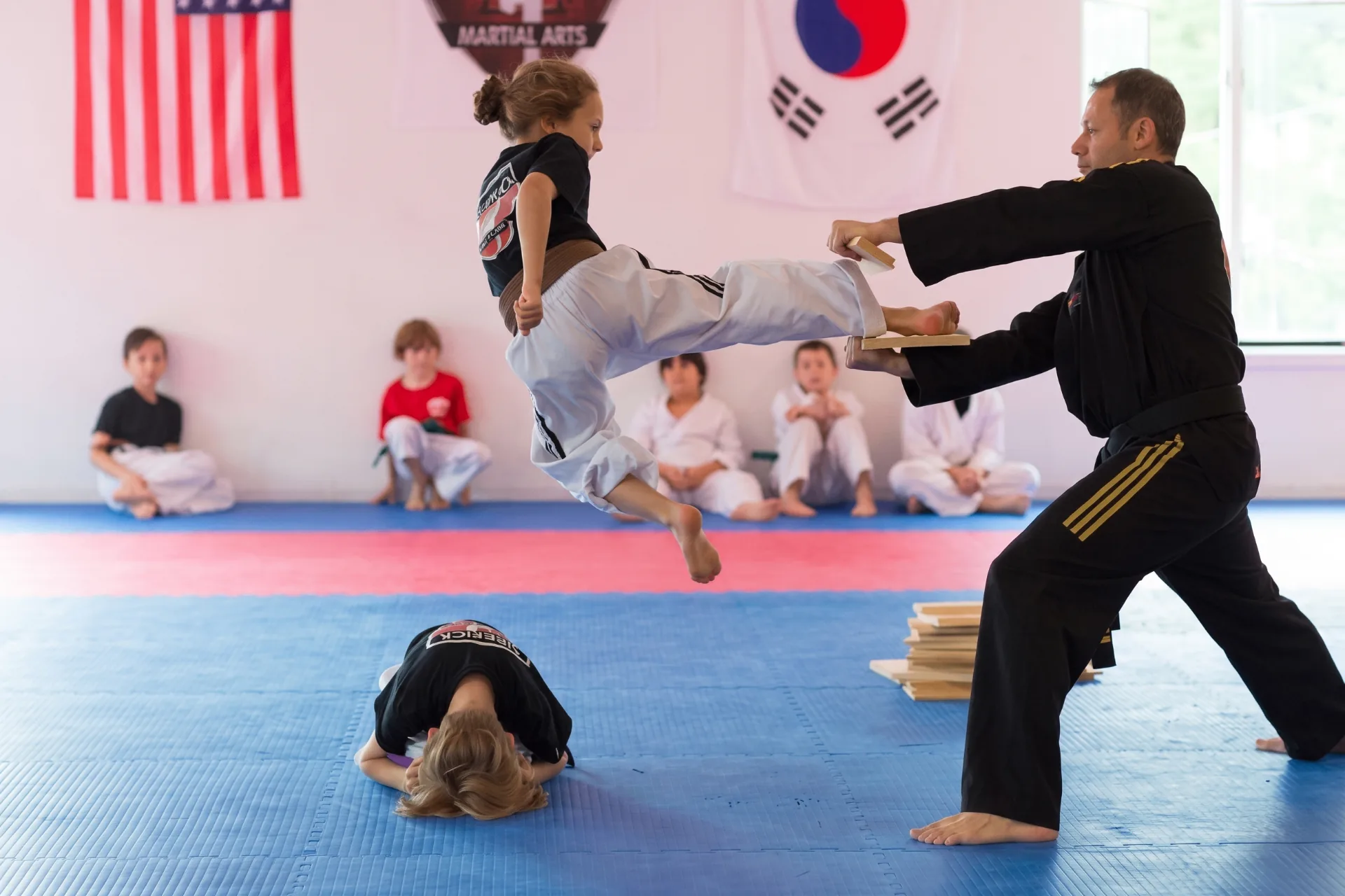 Student jumping over a classmate to break a board held by the instructor at Sidekick Martial Arts in Hasbrouck Heights, NJ